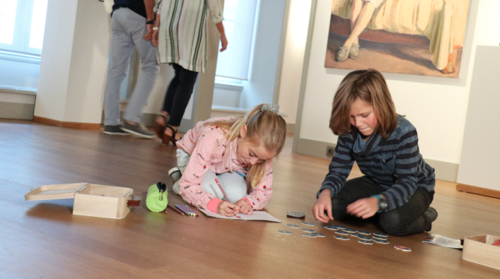 Twee kinderen zitten op de grond in het museum en spelen een spelletje