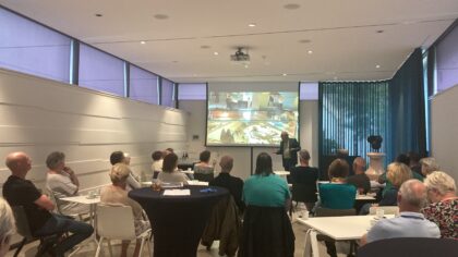 Een groep mensen in de zaal luisteren naar de spreker.